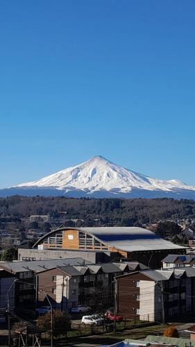 a snow covered mountain in the distance behind a building at Depto hermosa vista al Lago y Volcán in Villarrica