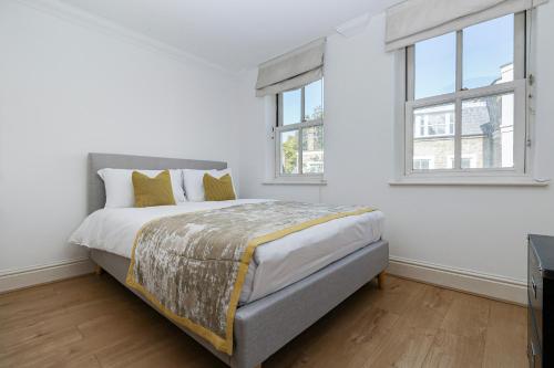 a white bedroom with a bed and two windows at Two bed Two bath Kensington Apartment in London