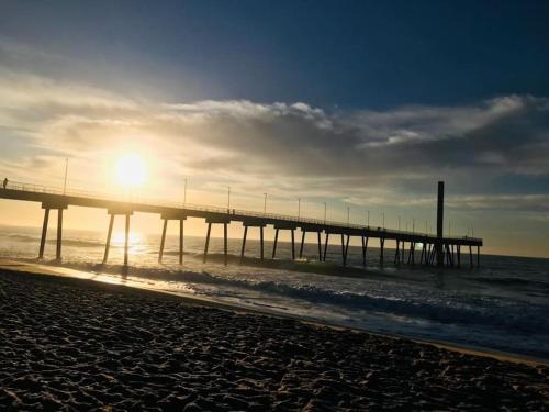 a pier on the beach with the sun rising over the ocean at Apartamento encantador em Rio das Ostras in Rio das Ostras