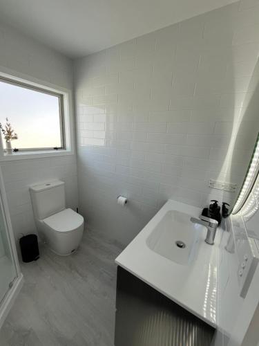 a white bathroom with a toilet and a sink at Papamoa Family Beach House in Tauranga