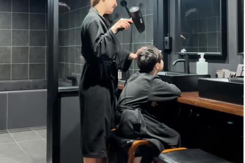 a woman blow drying a boys hair in a bathroom at Black Villa Naha 最大8名宿泊可 136平米 美栄橋駅 徒歩1分 in Tomari
