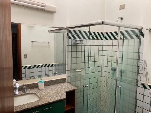 a bathroom with a glass shower with a sink and a mirror at Casa grande, ampla, com 4 quartos e estacionamento in Ribeirão Preto