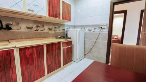 a kitchen with red wooden cabinets and a refrigerator at رؤى القنفذة للشقق المخدومة in Al Qunfudhah