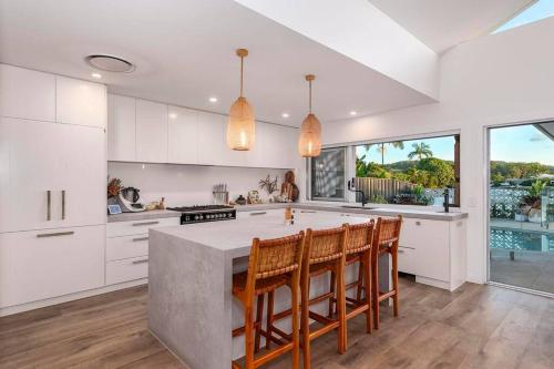 una cocina con armarios blancos y una gran isla con sillas en Luxe Modern Waterfront 4BR Oasis Wifi, BBQ & Pool, en Gold Coast