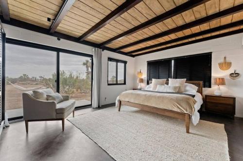Un dormitorio con una cama y una silla y ventanas. en The Desert Serenity-Stunning views-Pool-Spa-BBQ, en Yucca Valley
