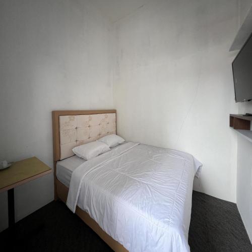 a small white bedroom with a bed and a desk at AN Homestay Syariah Mitra RedDoorz Wonosobo in Wonosobo