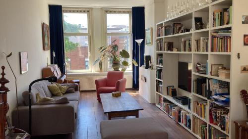 a living room with a couch and a table and book shelves at Mooi Appartement in Kralingen in Rotterdam