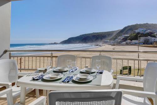 a table with glasses and plates on a balcony with the beach at Makarios On Sea in Herolds Bay
