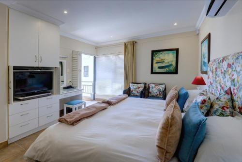 a bedroom with a large white bed and a television at Makarios On Sea in Herolds Bay