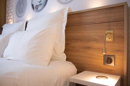 a bed with white pillows and a wooden headboard at Brit Hotel Limoges Centre Gare - Hôtel & Spa in Limoges