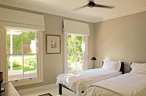 two beds in a bedroom with two windows at Kumbuk House in Franschhoek