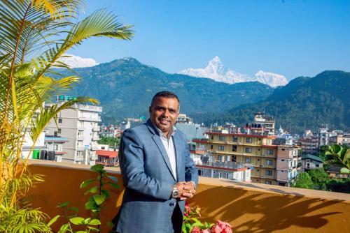 a man standing on a balcony with mountains in the background at Hotel Hidden Kingdom in Pokhara