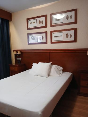 a bedroom with a white bed with pictures on the wall at Hostal Los Infantes in Olvega