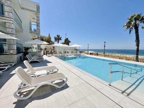a swimming pool with lounge chairs and the ocean at Hotel Apartamentos Marina Luz in Chipiona