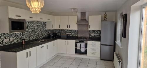 a kitchen with white cabinets and a stainless steel refrigerator at 4-Bed Charming Pet-Friendly House w Garden in Peterborough
