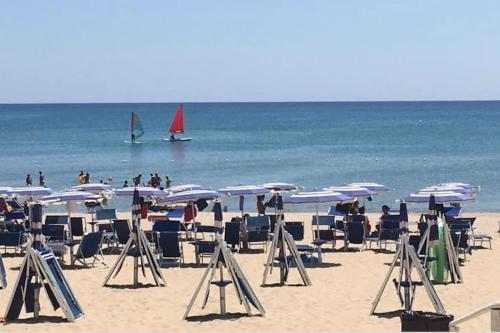a beach with chairs and umbrellas and a boat in the water at Chalet Felicita con giardino Immerso nel bosco in Castellaneta Marina 
