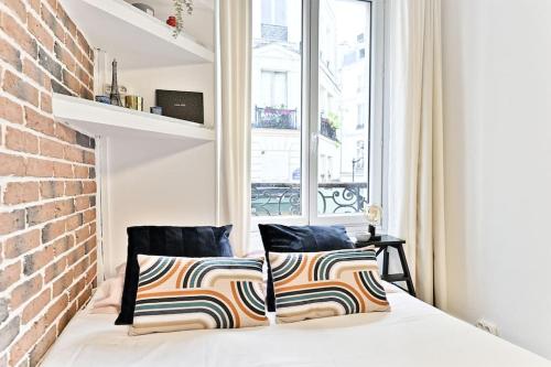 Cette chambre dispose d'un lit avec deux oreillers et d'un mur en briques. dans l'établissement Petit studio confortable et central #marais - II, à Paris