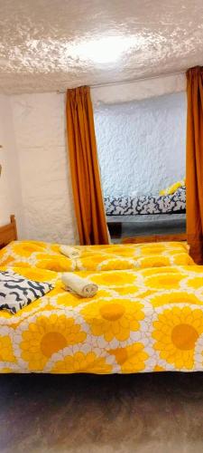 a bed with a yellow and white comforter and a window at Casa Cueva Rural Trébola, Artenara in Juncalillo