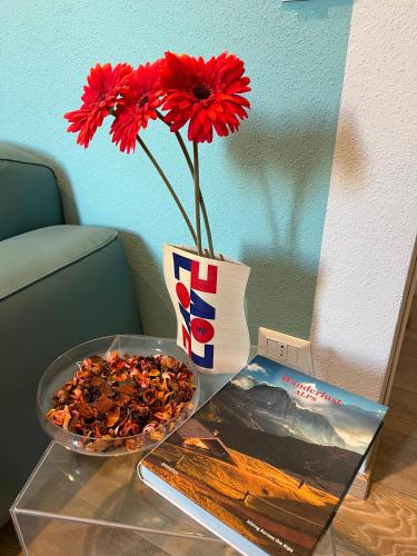 a table with a vase with red flowers and a book at Villa Italia in Canzo
