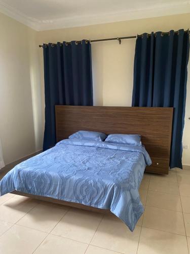 a bedroom with a bed with blue sheets and blue curtains at Kyanja 2 BDRM Apartment in Buwate