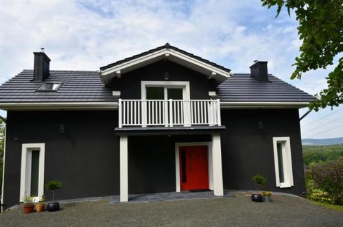 a black house with a red door and a balcony at Siedlisko na Agatowej w Rudnie in Rudno