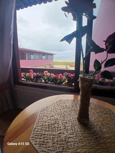 a table with a vase with a flower in a window at Recanto Pequena Sereia in São Mateus