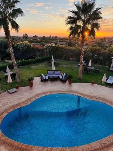 a large blue swimming pool with a sunset in the background at Villa Diaf Johanne in Aït Ourir