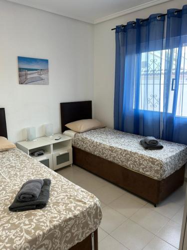 ロス・アルカサレスにある3 bed villa, large private pool 10 mins walk from beach and amenitiesのベッドルーム1室(ベッド2台、青いカーテン付きの窓付)