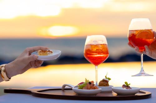 a person holding a plate of food and two glasses of wine at Baglioni Resort Maldives - Luxury All Inclusive in Dhaalu Atoll
