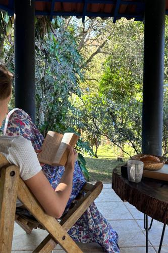 a person sitting in a chair reading a book at Casa na Serra para 14 Pessoas com Piscina e Churrasqueira - Da Francesa in Bom Jardim