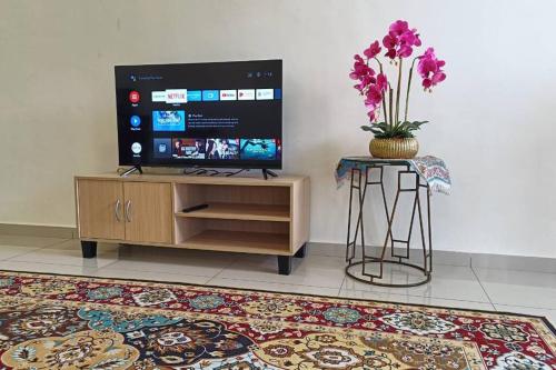 a living room with a tv and a table with a vase of flowers at Sri Keroma Bajandoh Muar Homestay in Muar