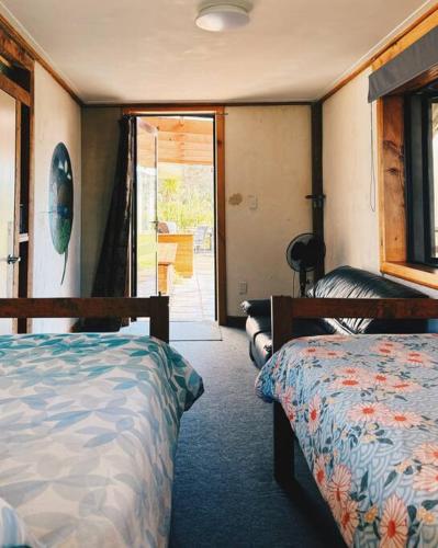a bedroom with two beds and a door to a patio at Wake up and Thrive in Raglan