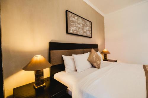a bedroom with a white bed with a lamp on a table at Sarinande Hotel in Seminyak
