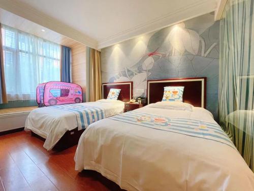 a hotel room with two beds and a pink suitcase at 无锡东方枫韵商务酒店惠山万达店 in Mazhen