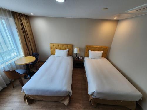 two beds in a hotel room with a desk and a table at Hotel Haema in Jeju