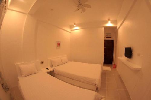 a small white room with two beds and a tv at Coron Bluewave Hotel in Coron