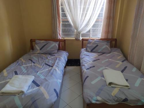 two beds in a small room with a window at Antonio Accommodation Nakuru in Nakuru
