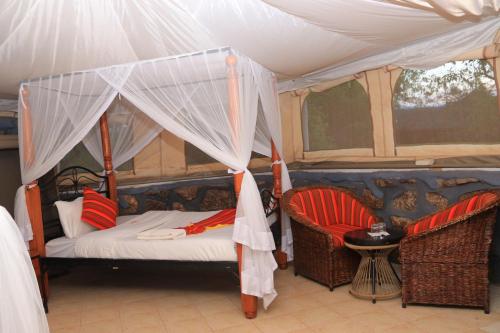 a bedroom with a canopy bed and two chairs at ELANGATA OLERAI LUXURY TENTED CAMP in Narok