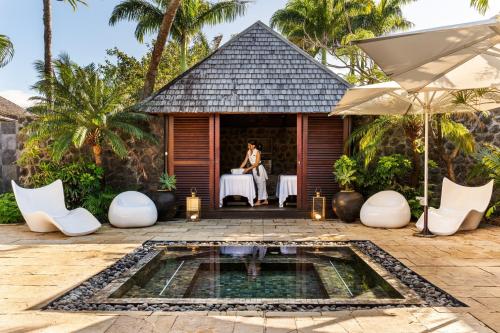 a woman sitting at a table outside a house with a pool at Palm Hotel & Spa in Petite Île