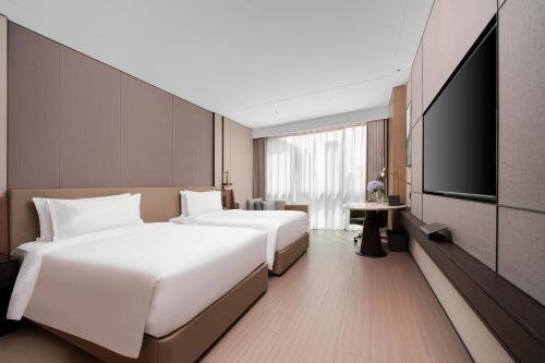 two beds in a hotel room with a flat screen tv at Grand Mercure Wuhan Hanyang in Wuhan
