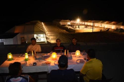 a group of people sitting around a table at night at Aroma Desert Safari Camp in Sām