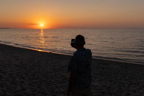 a man taking a picture of the sunset on the beach at Q Resort in Marina di Sorso