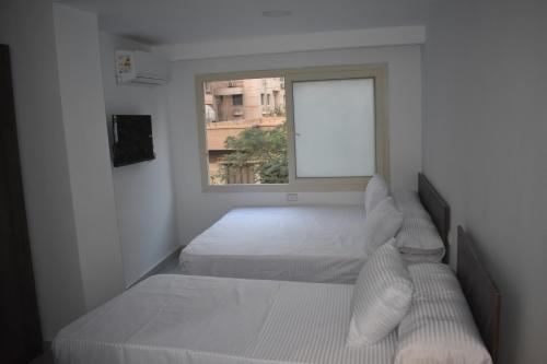 a white bedroom with two beds and a window at villa 17 in Cairo