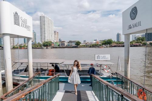a woman in a dress standing on a dock next to a boat at The Salil Hotel Riverside Bangkok in Bangkok