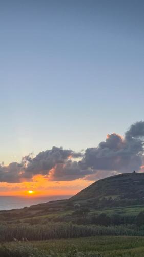 a sunset over a green field with the sun setting on the horizon at Vivenda Flor in Ponta Delgada