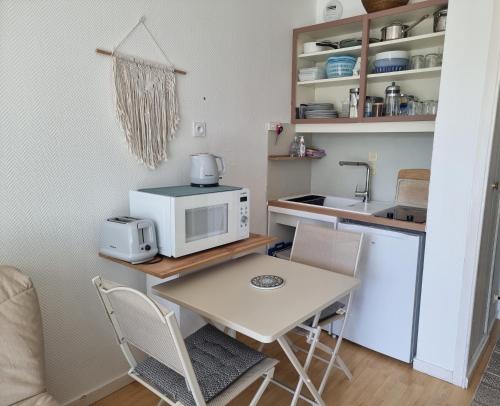 une petite cuisine avec une table et un micro-ondes dans l'établissement Studio, balcon et accès direct page, à Dinard