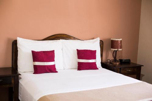 1 dormitorio con 1 cama con almohadas rojas y blancas en La Bellota Hotel en Siguatepeque