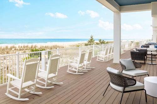 a deck with white chairs and tables and the beach at Hilton Garden Inn Ocean City Oceanfront in Ocean City