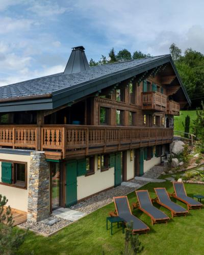 une maison avec une terrasse et des chaises sur la pelouse dans l'établissement Chalet Molitor, avec services, Collection Chalets des Fermes, à Megève