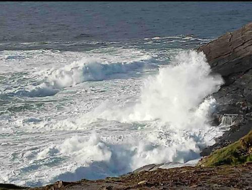 a wave crashing on the rocks near the ocean at Rose Cottage in Inagh